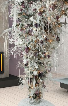 a tall white christmas tree with ornaments and lights on it's branches in front of a fireplace