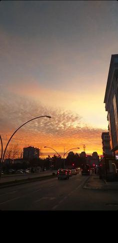 the sun is setting over a city street with cars driving down it's side