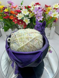 a ball of yarn sits in a purple basket on a plate next to colorful flowers