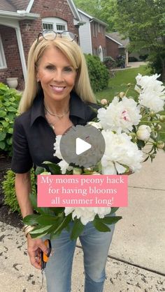 a woman standing in front of a house holding flowers and a sign that says, my moms peony back for having blooms all summer long