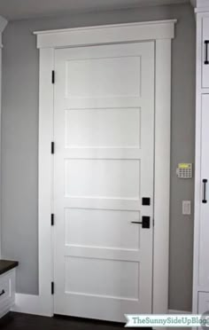 a white door in the corner of a room with gray walls and wood flooring