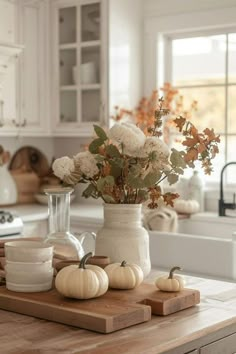 a wooden cutting board topped with flowers and pumpkins on top of a kitchen counter