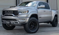 a silver ram truck parked in front of a garage door with black rims and tires