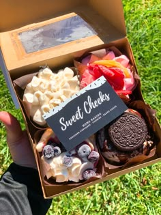 a box filled with different types of desserts on top of green grass next to a persons hand