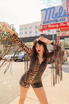 The Leopard Fringe Romper is a disco-meets-cowboy dream come true. Its dreamy details include a zip-up front and fringe along the sleeves. Born to live its best life on the dance floor. Be prepared for nonstop compliments.   Form-fitting, makes your booty look A+ Carefully hand-cut velvet fringe tassels Fabric: Made wi Disco Denim, Desert Disco, Disco Cowboy, Printed Bell Bottoms, Fringe Romper, Sequin Flare Pants, Cowboy Outfit, Rhinestone Cowboy, Velvet Fringe