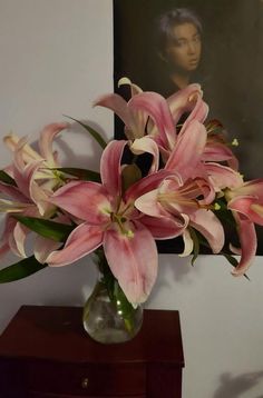 a vase filled with pink flowers sitting on top of a wooden table next to a painting