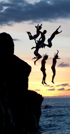 people jumping off rocks into the ocean at sunset