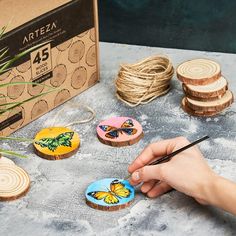 a person is painting wooden slices with butterflies on them and other items around the table