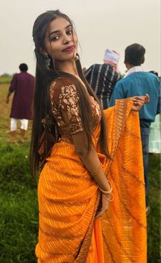 a woman in an orange sari is posing for the camera with other people behind her