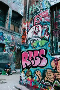 graffiti on the side of a building in an alleyway with people sitting and walking