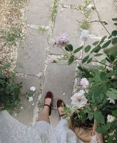 a woman's feet with red shoes standing next to pink flowers and greenery