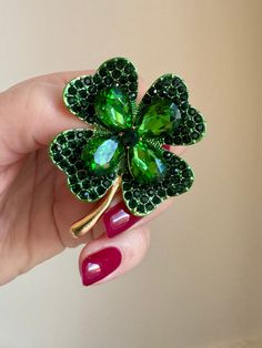 a woman's hand holding a green brooch with four leaf clovers on it