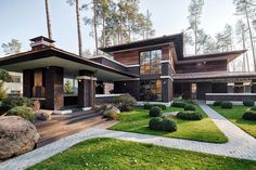 a modern house in the woods with green grass and rocks on the front lawn, surrounded by trees