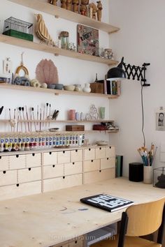 a wooden table topped with lots of crafting supplies next to shelves filled with items