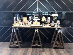 two wooden tables with cakes and other items on them in front of a black wall