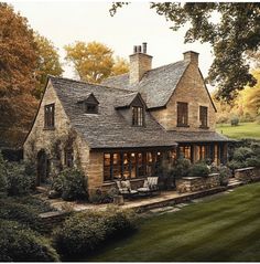 a stone house with an outdoor seating area in the foreground and trees surrounding it