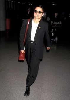 a man in a suit and sunglasses is walking through an airport with his hand on his hip