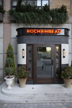 an entrance to a restaurant with potted plants on the outside and lights above it