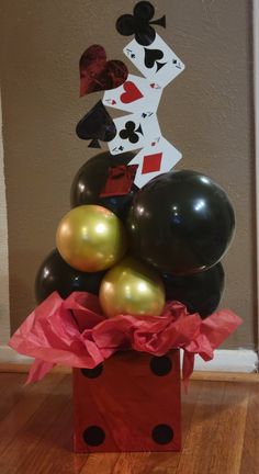 some balloons are in a red box on the floor and one is black with gold foil