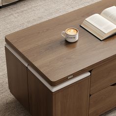 a cup of coffee and an open book sit on a table with drawers in front of it