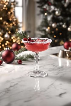 a red drink in a glass on a table with christmas decorations and trees behind it