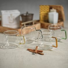 three glass mugs with cinnamon sticks in them on a table next to other items