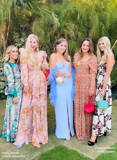 four women standing next to each other in long dresses and one is holding a purse