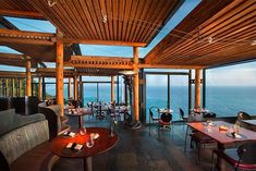 an outdoor restaurant overlooking the ocean with wooden ceilings and tables set up for two people