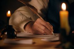 a person writing on paper with candles in the background