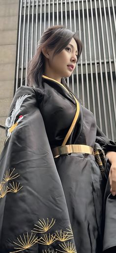 a woman dressed in black and gold is standing next to a building with her hand on her hip