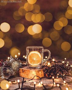 a glass cup with an orange slice in it on a wooden table surrounded by christmas lights