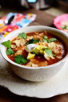 a bowl of soup with tortilla chips and sour cream in it on a plate