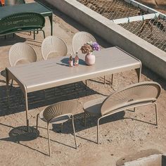 an outdoor table with four chairs and a vase of flowers on the ground next to it