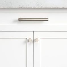 a white cabinet door with two knobs and a metal handle on the bottom drawer