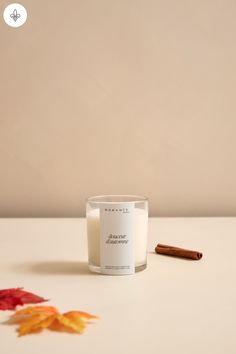 a glass candle with cinnamon sticks next to it on a white tablecloth and some autumn leaves