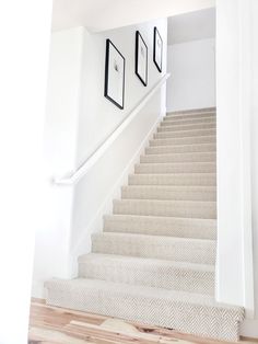 a staircase with white carpet and black framed pictures on the wall