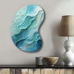 an abstract painting on the wall next to a lamp and table with a vase in front of it