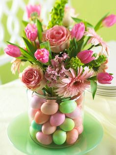 a vase filled with pink flowers and eggs on top of a green saucer covered in candy