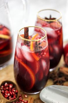 two glasses filled with red wine and pomegranates on top of a cutting board