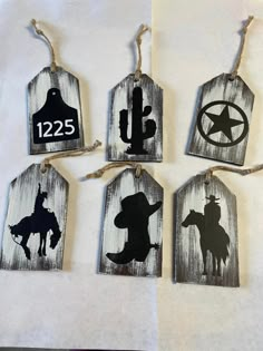 four tags with cowboy silhouettes on them are hanging from twine string and decorated with rope