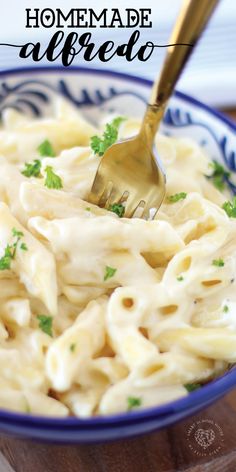 a bowl filled with pasta and parsley on top of a wooden table next to a fork