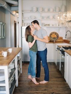 a man and woman standing in the middle of a kitchen with open shelves on either side