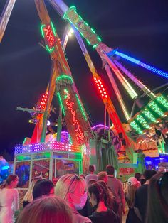 a carnival ride at night with people standing around it and lights on the rides are brightly colored