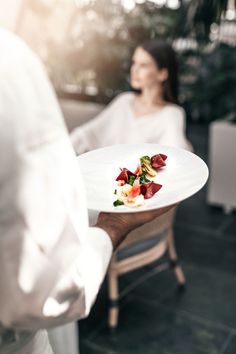 a person holding a plate with food on it in front of a woman sitting at a table