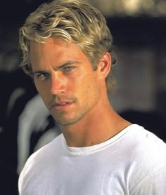 a man with blonde hair wearing a white t - shirt and looking at the camera