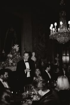 a black and white photo of a man in a tuxedo at a dinner table