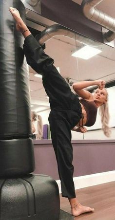 a woman standing on one leg and doing a handstand in front of a punching bag