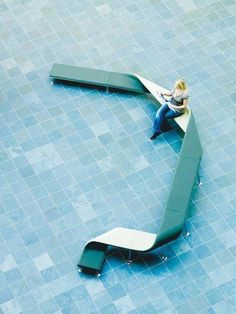 a woman sitting on a bench in the middle of a tiled floor with an arrow shaped bench next to her