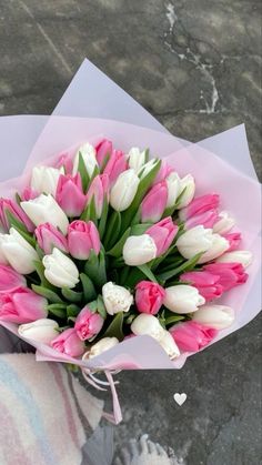 a bouquet of pink and white tulips in someone's hand on the ground