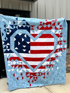 an american flag heart quilt hanging on the side of a building in front of a garage